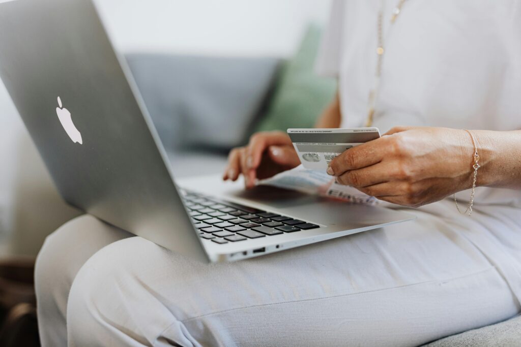 Cliente faz checkout de compra online com cartão de crédito em notebook no colo, com as mãos sobre o teclado.
