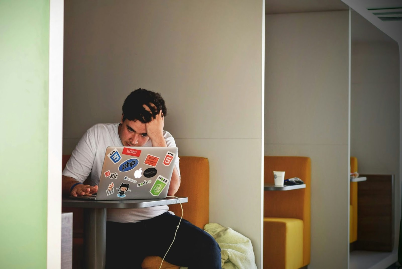 Um desenvolvedor jovem, com a mão na cabeça, em um momento de estresse ou concentração profunda, trabalhando em seu notebook para corrigir problemas no processo de checkout. A tela do notebook não está visível.
